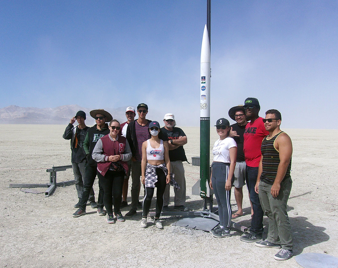 Imua team standing in the desert next to their 12 foot tall rocket