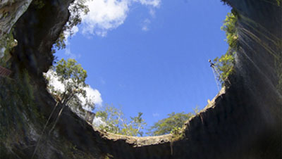 Looking up from inside a cave to a hole in the top at a blue sky