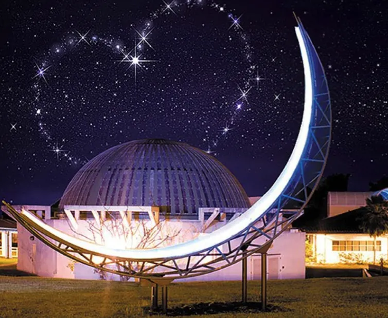 Moon sculpture lit up at night with stars in the sky forming a heart