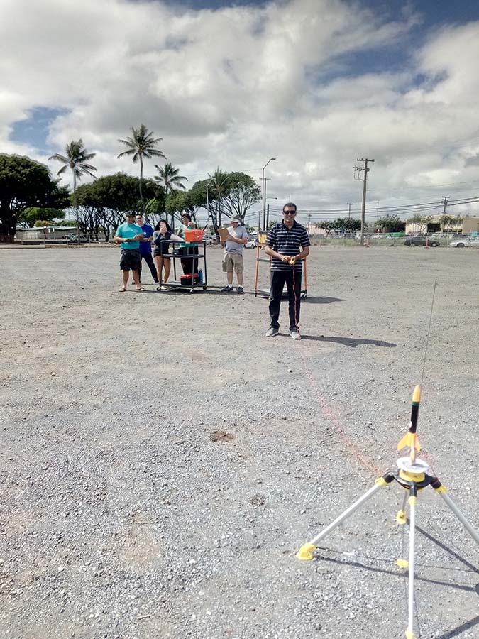 students in a gravelly lot ready to launch a small rocket