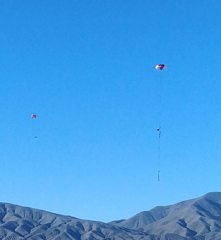 chute and payload descending from the sky with desert mountains in background